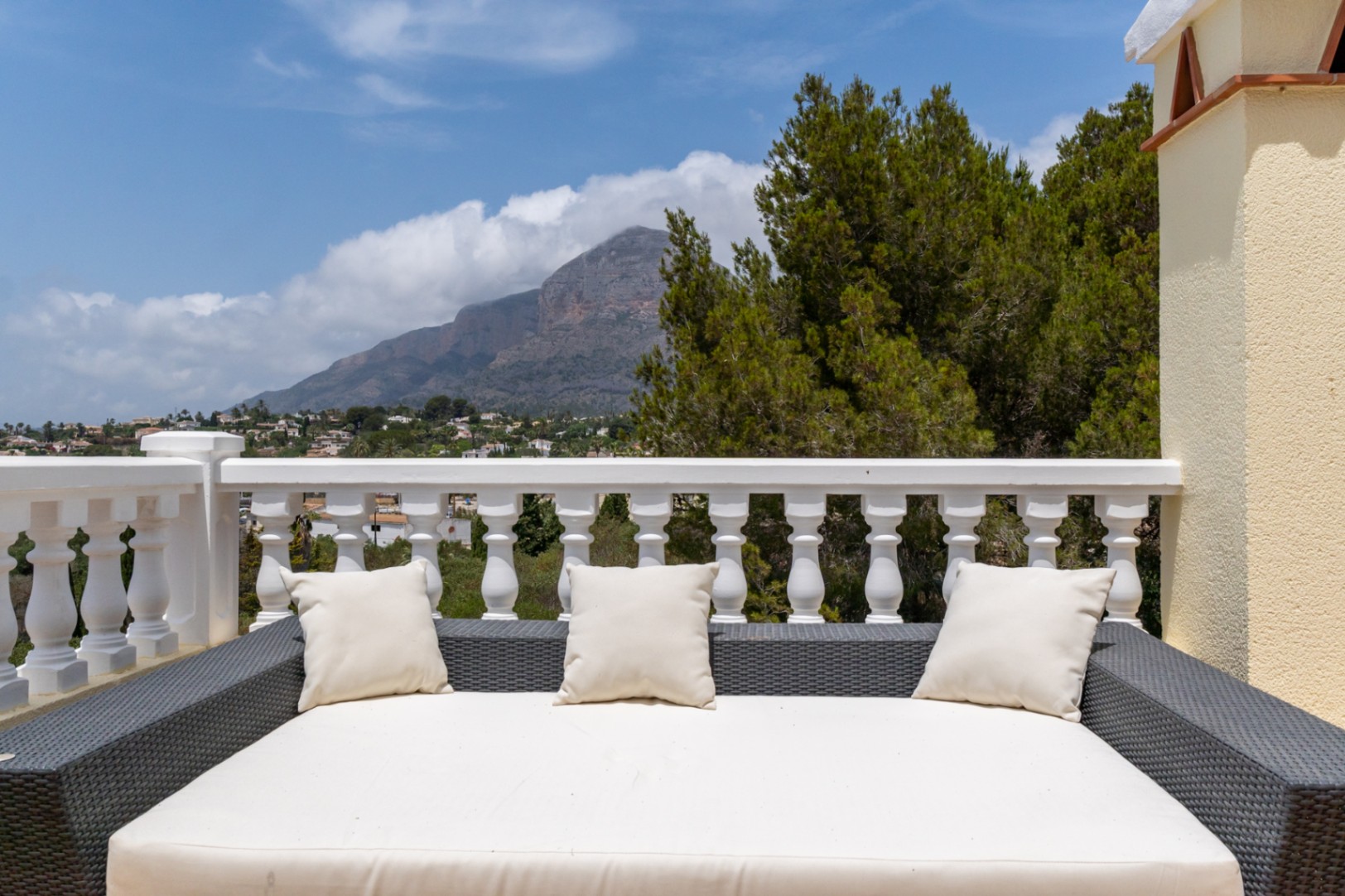 Bovenste terras voorzien van een groot rotan ligbed en witte balustrade, met een panoramisch uitzicht op de berg Montgó en de vallei.
