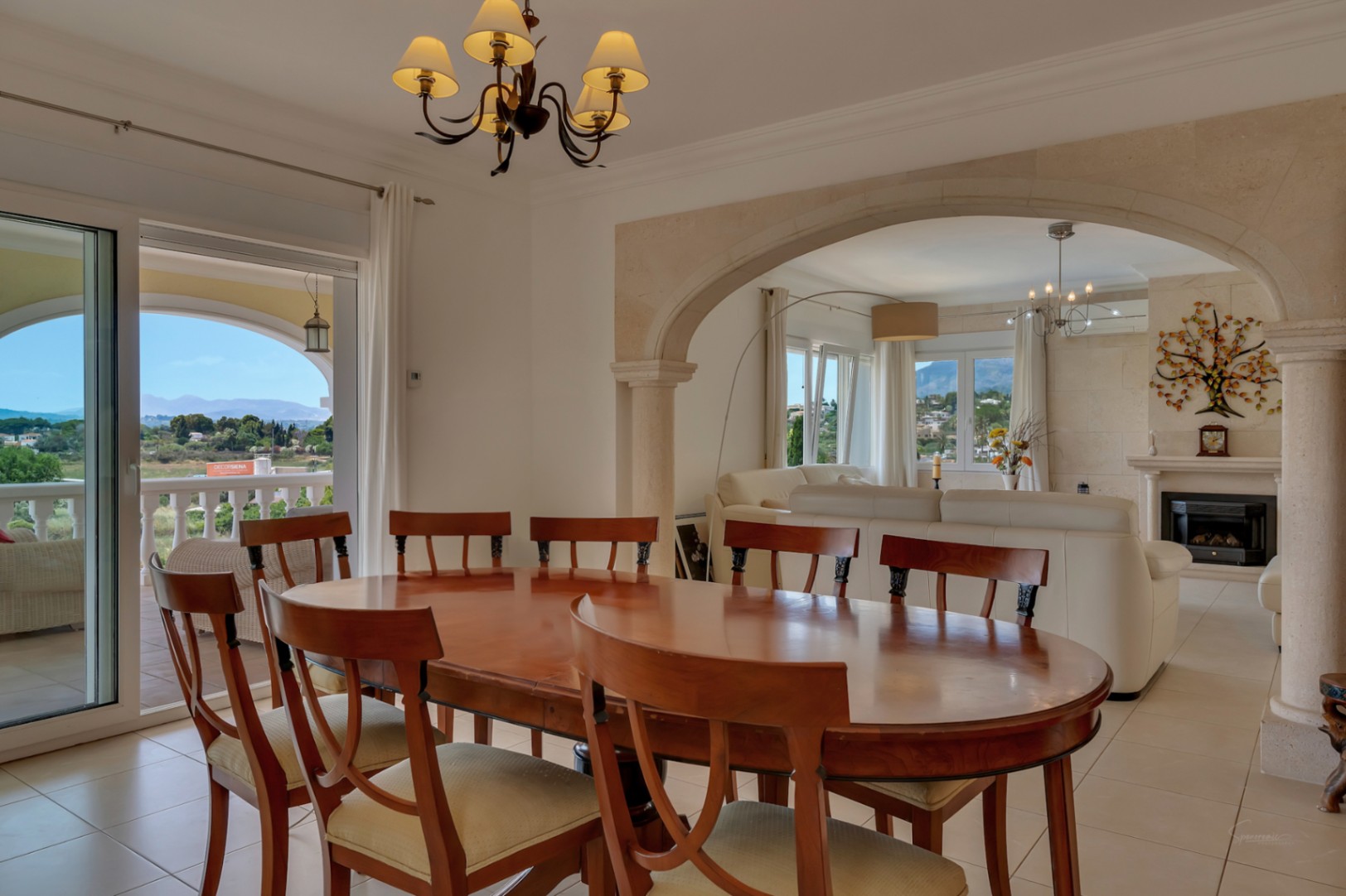 Eetkamer met hardhouten tafel en Tosca natuurstenen boog naar de woonkamer, met toegang tot het terras en panoramisch uitzicht op de vallei.