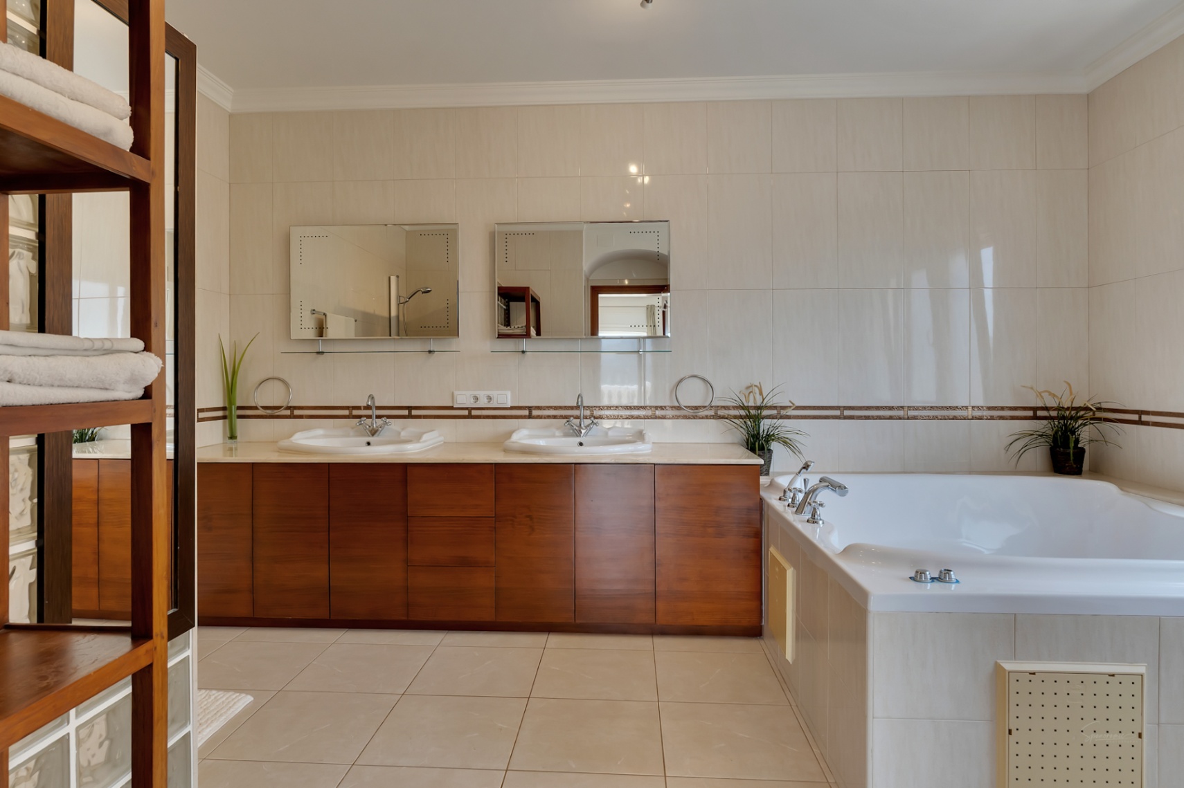 En-suite badkamer met dubbel houten wastafelmeubel, ingebouwd hydromassagebad en wandtegels in neutrale crèmetinten met decoratieve randen.