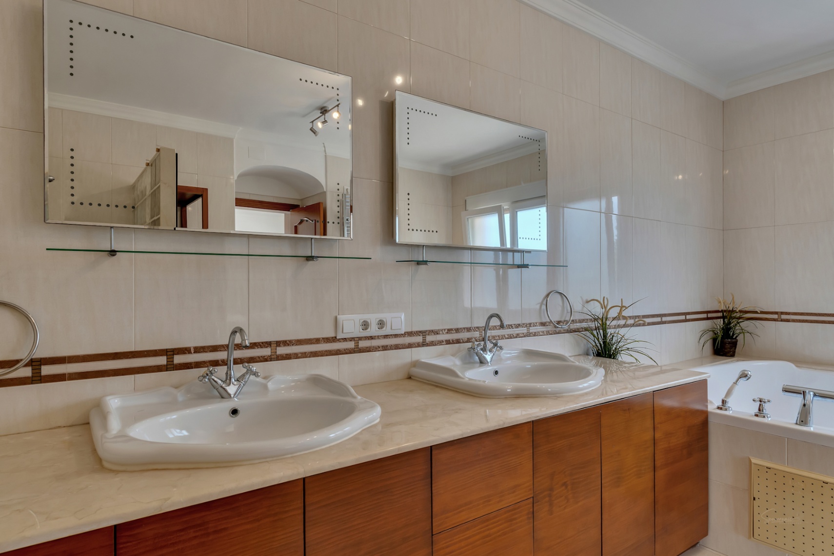 En-suite badkamer met dubbele wastafel op een marmeren blad, houten kasten en achterverlichte spiegels naast het hydromassagebad.