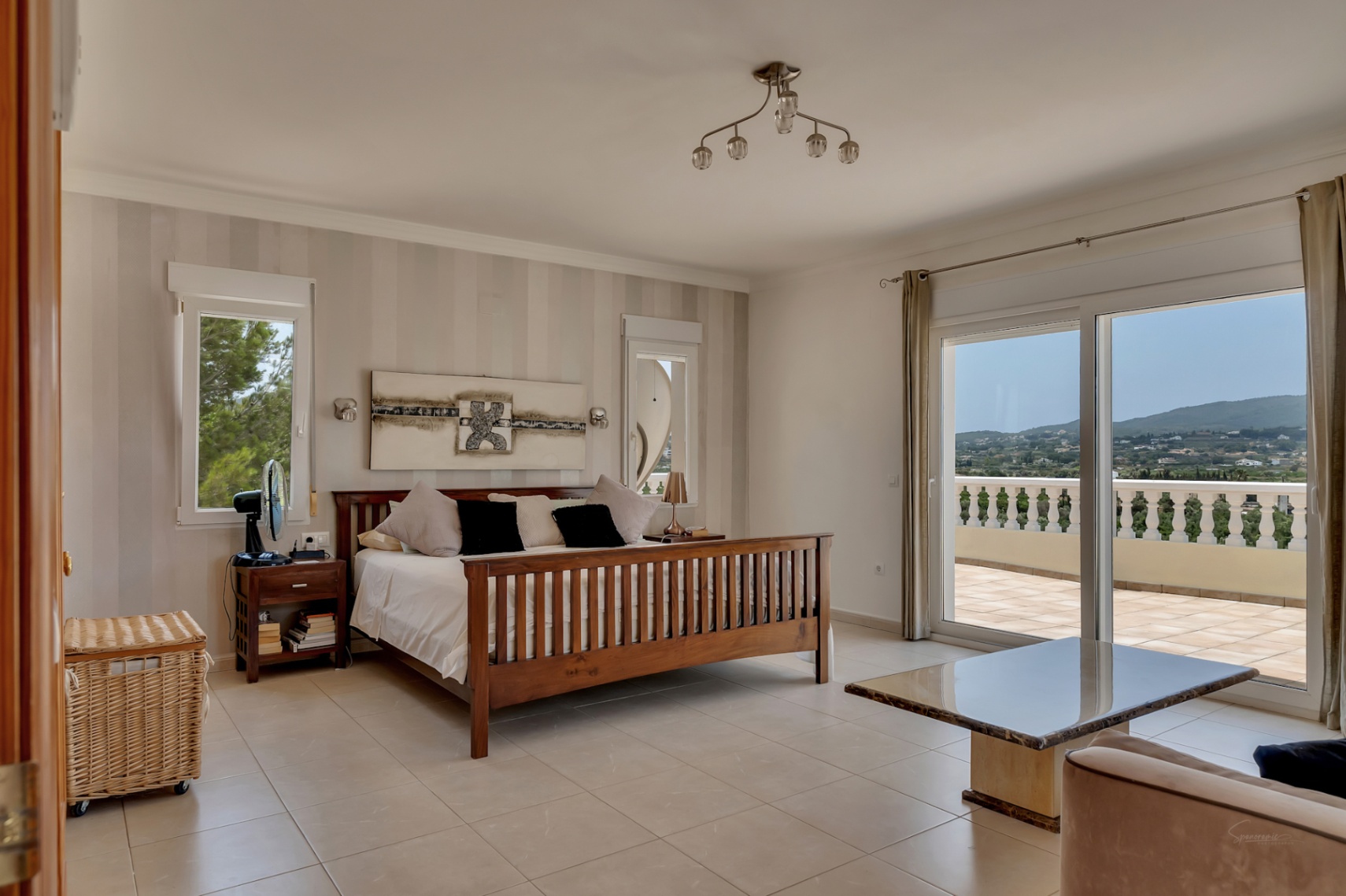 Hoofdslaapkamer met houten bedframe, gestreept behang en grote glazen schuifdeuren die toegang bieden tot een terras met panoramisch uitzicht over de vallei.