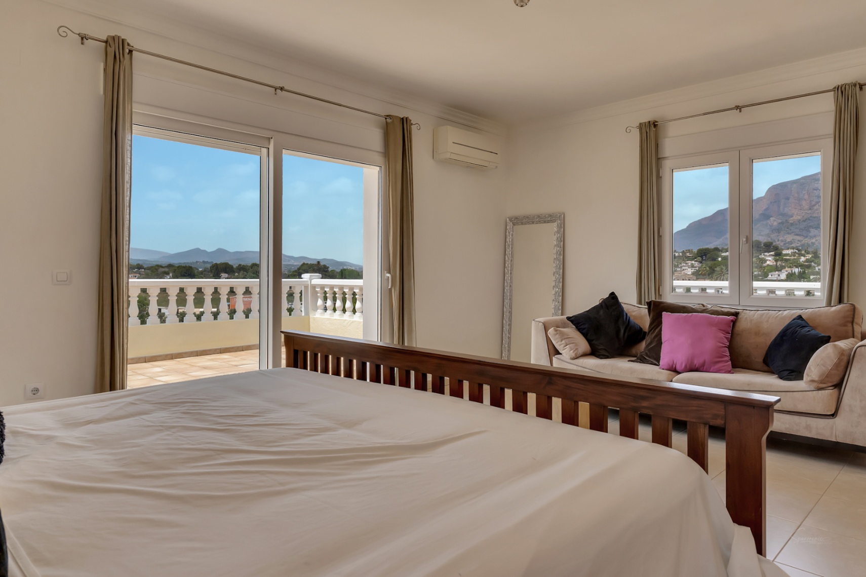 Hoofdslaapkamer met houten bedframe, zithoek en schuifpui naar het terras met panoramisch uitzicht op de Montgó en de omliggende vallei.