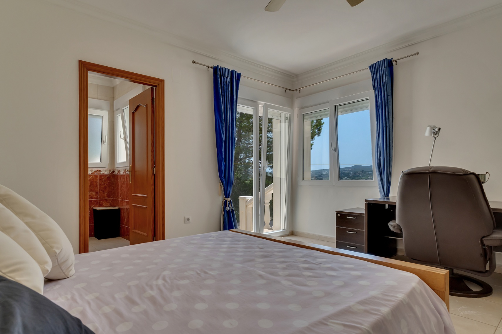 Lichte slaapkamer met werkplek, en-suite badkamer en toegang tot het terras. Grote ramen bieden een panoramisch uitzicht over de omliggende heuvels.