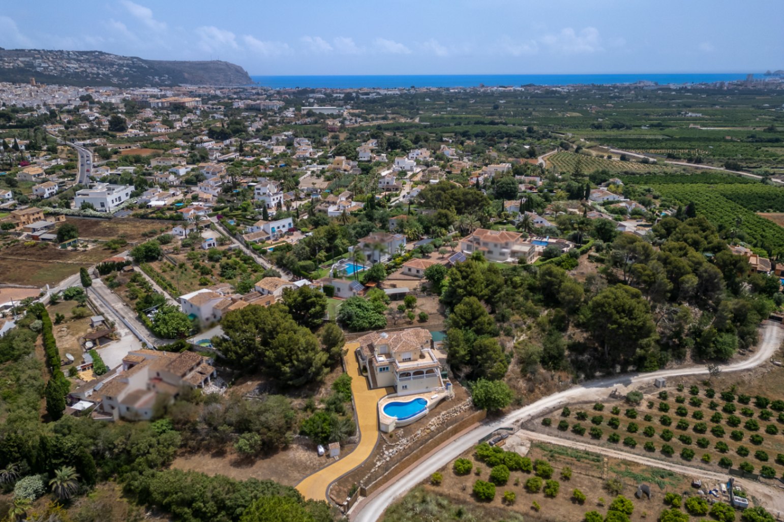 Luchtfoto van de villa met de verhoogde ligging, het overloopzwembad en de oprit, met een panoramisch uitzicht over de vallei van Jávea en de Middellandse Zee.