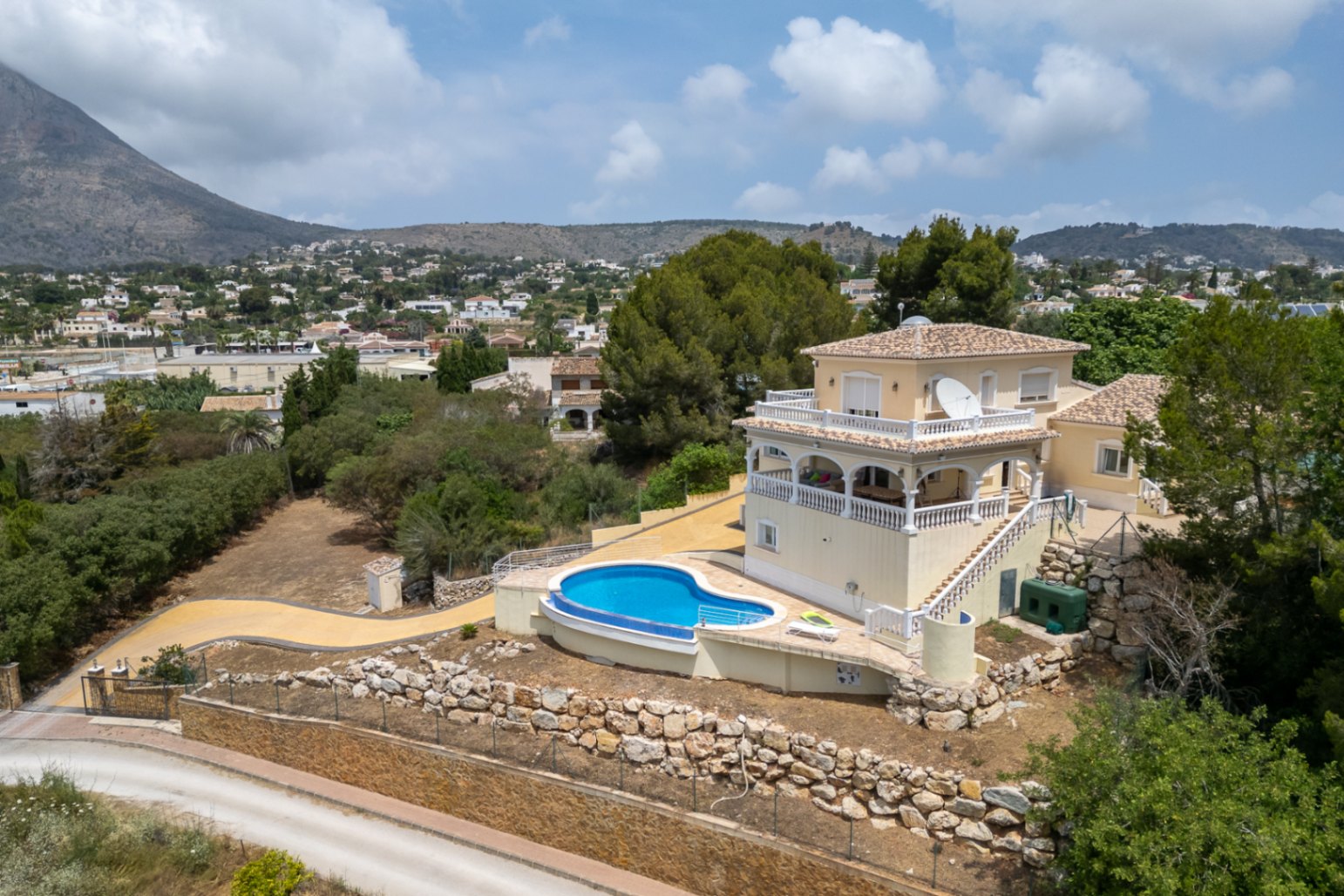 Luchtfoto van de villa met gebogen zwembad, naya met bogen en terrassen met balustrades, met een panoramisch uitzicht over de vallei en de Montgó.