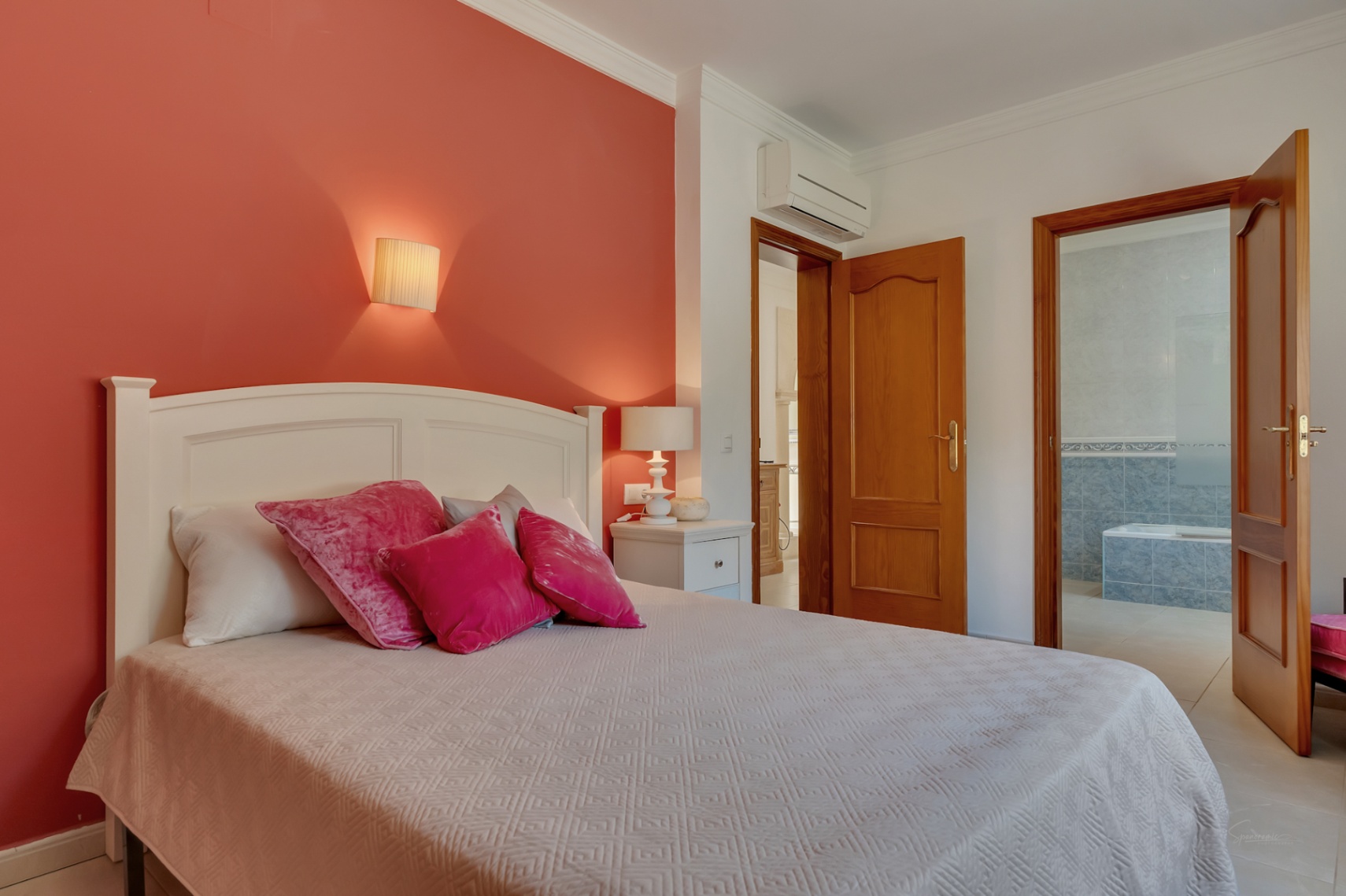 Slaapkamer met een terracotta accentmuur, split-unit airconditioning en toegang tot een en-suite badkamer met blauwe tegels en ligbad.