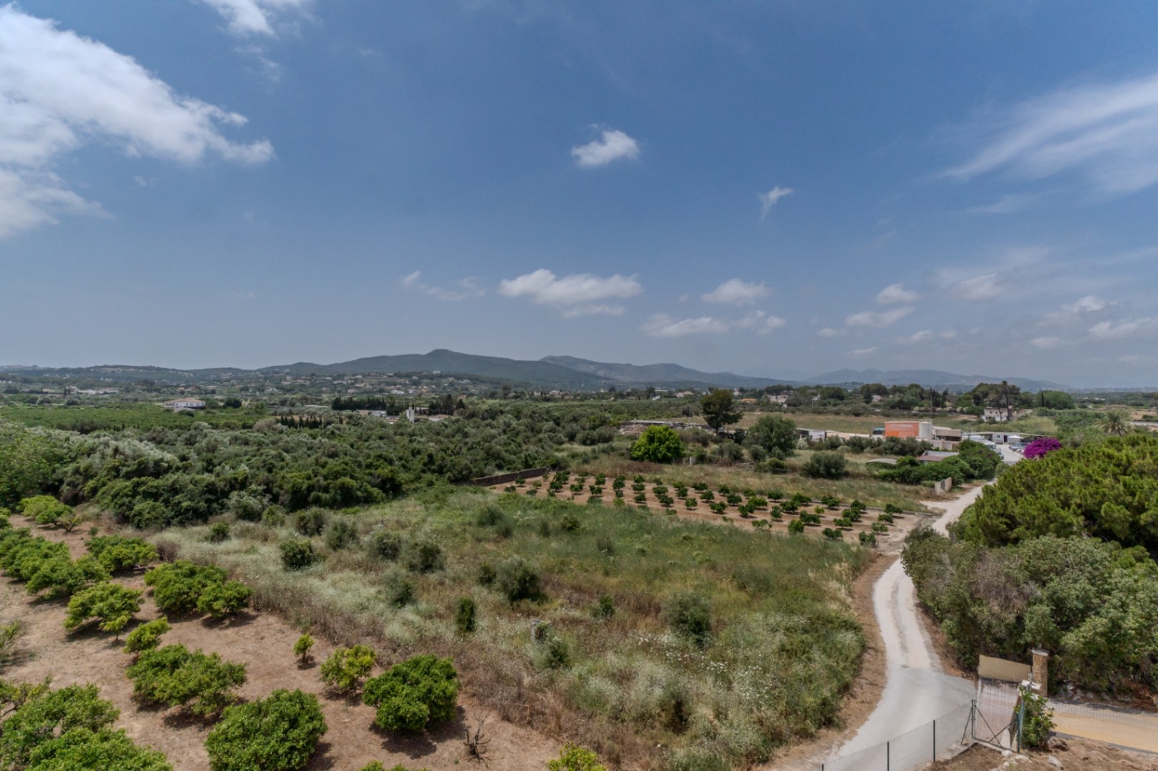 Verhoogd 180-graden panoramisch uitzicht over de vallei van Jávea, met agrarische boomgaarden en de heuvels van Benitachell in de verte.