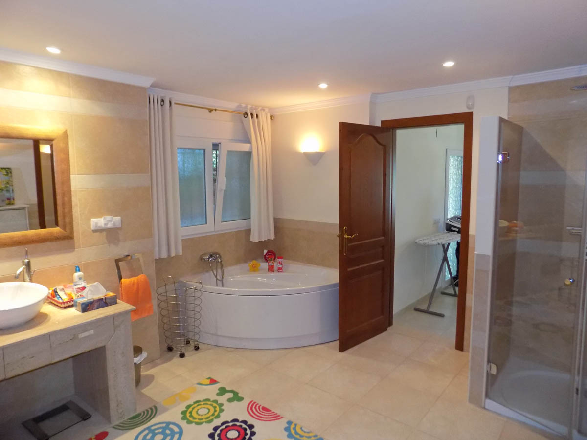 Badkamer met hoekjacuzzi, aparte inloopdouche met glazen wand en een natuurstenen wastafelmeubel met opbouwkom en inbouwspots.