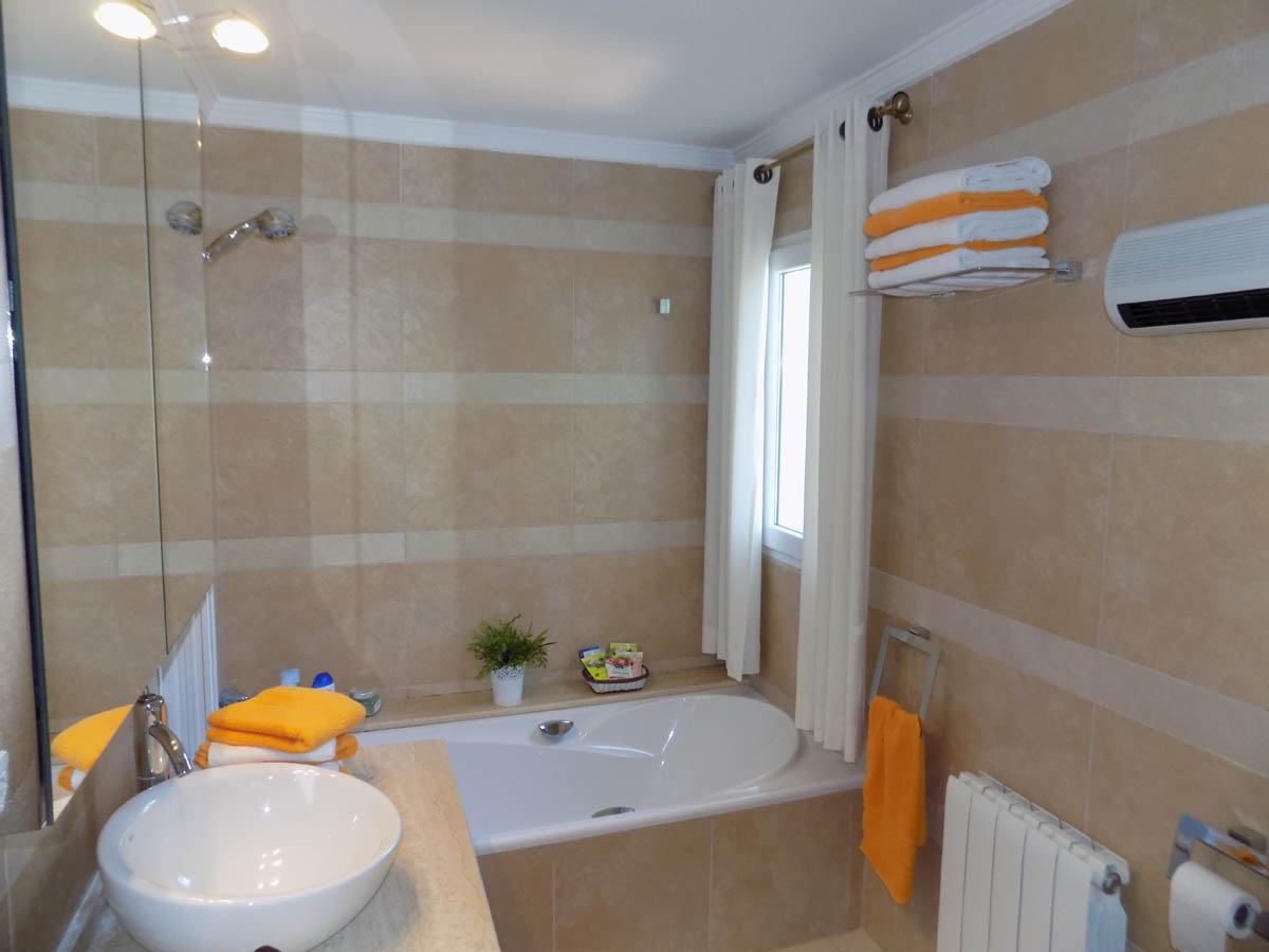 Badkamer met ingebouwd ligbad, een witte opzetwastafel op een natuurstenen blad en wanden met horizontaal gestreepte crèmekleurige tegels.