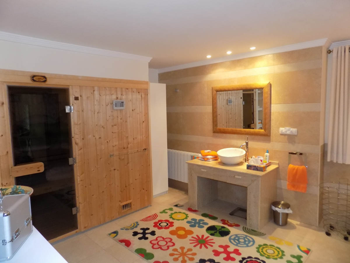 Badkamer met ingebouwde houten sauna, natuurstenen wastafelmeubel en wandtegels in warme tinten. Voorzien van inbouwspots en een radiator.