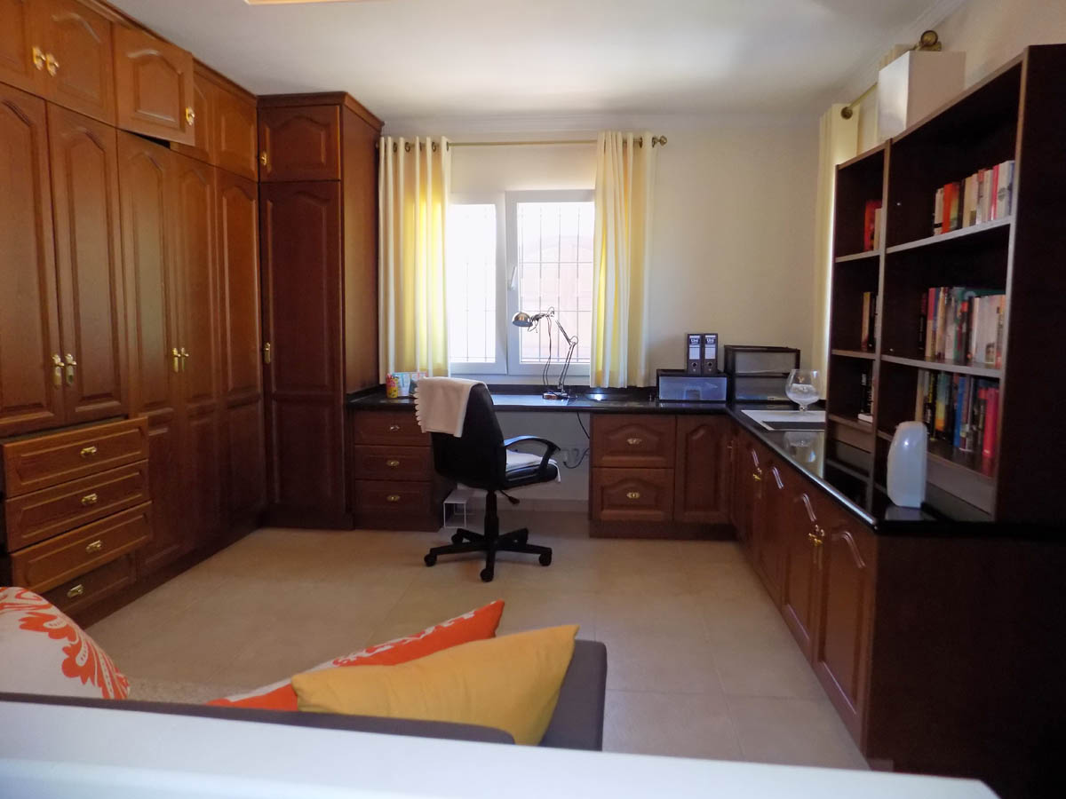Functioneel kantoor met uitgebreide houten inbouwkasten, een L-vormig bureau met donker werkblad en een geïntegreerde boekenkast.