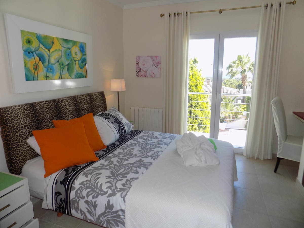 Lichte slaapkamer met directe toegang tot het terras, tweepersoonsbed met luipaardprint hoofdbord en uitzicht op de mediterrane tuin door grote glazen deuren.