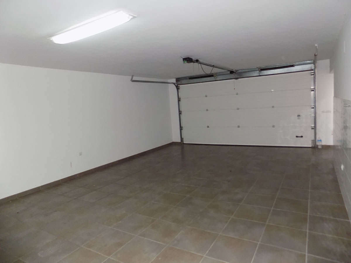 Ruime dubbele garage in het souterrain, voorzien van een tegelvloer, witte muren en een brede automatische sectionaaldeur.