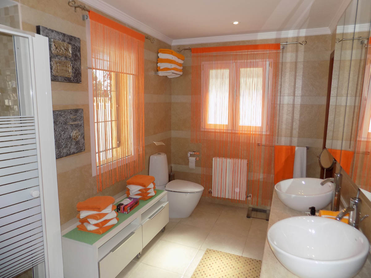 Volledige badkamer met dubbele opzetwastafel, beige gestreepte wandtegels en natuurlijke lichtinval via twee ramen.