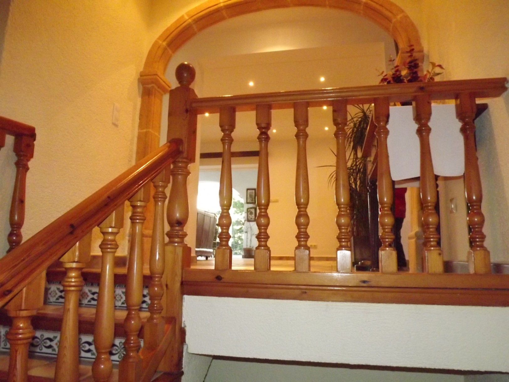 Binnentrap met gedraaide houten balustrade, decoratieve tegelstootborden en een natuurstenen boog die de toegang tot de bovenverdieping omlijst.