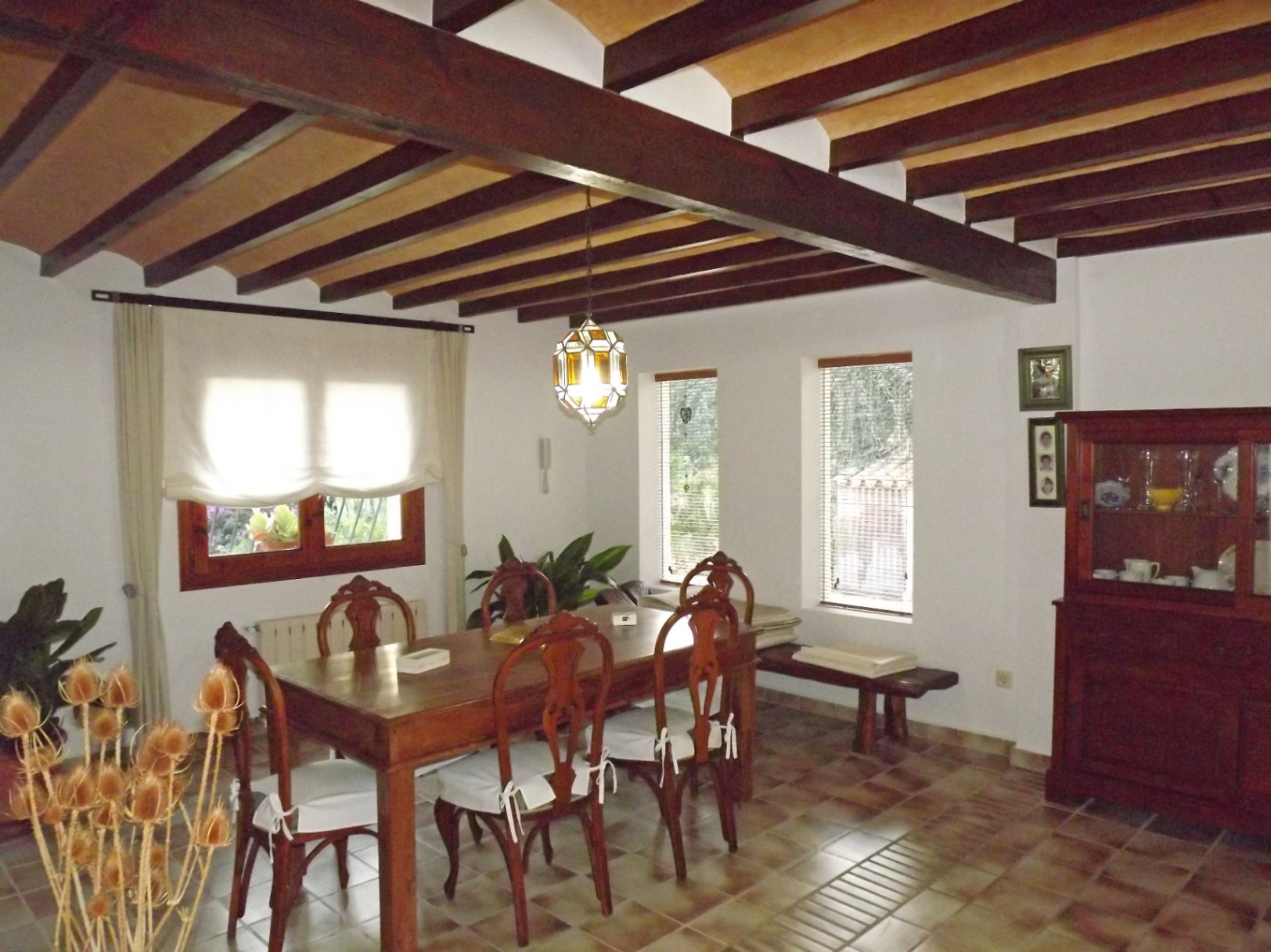 Rustieke eetkamer met zichtbare houten plafondbalken, een massief houten tafel met bewerkte stoelen en een traditionele tegelvloer.