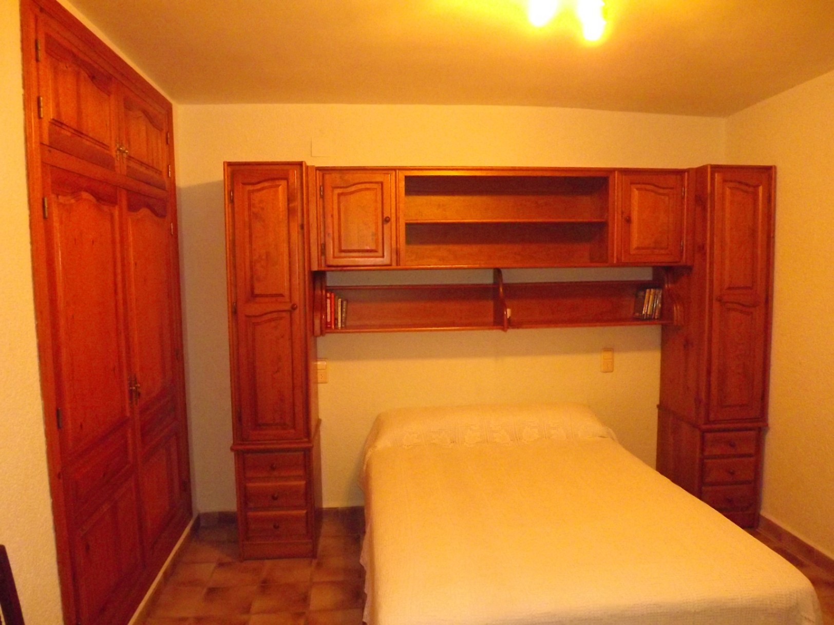 Slaapkamer met massief houten meubilair, inclusief een inbouwkast en een brugmeubel met planken en lades rondom het bed.