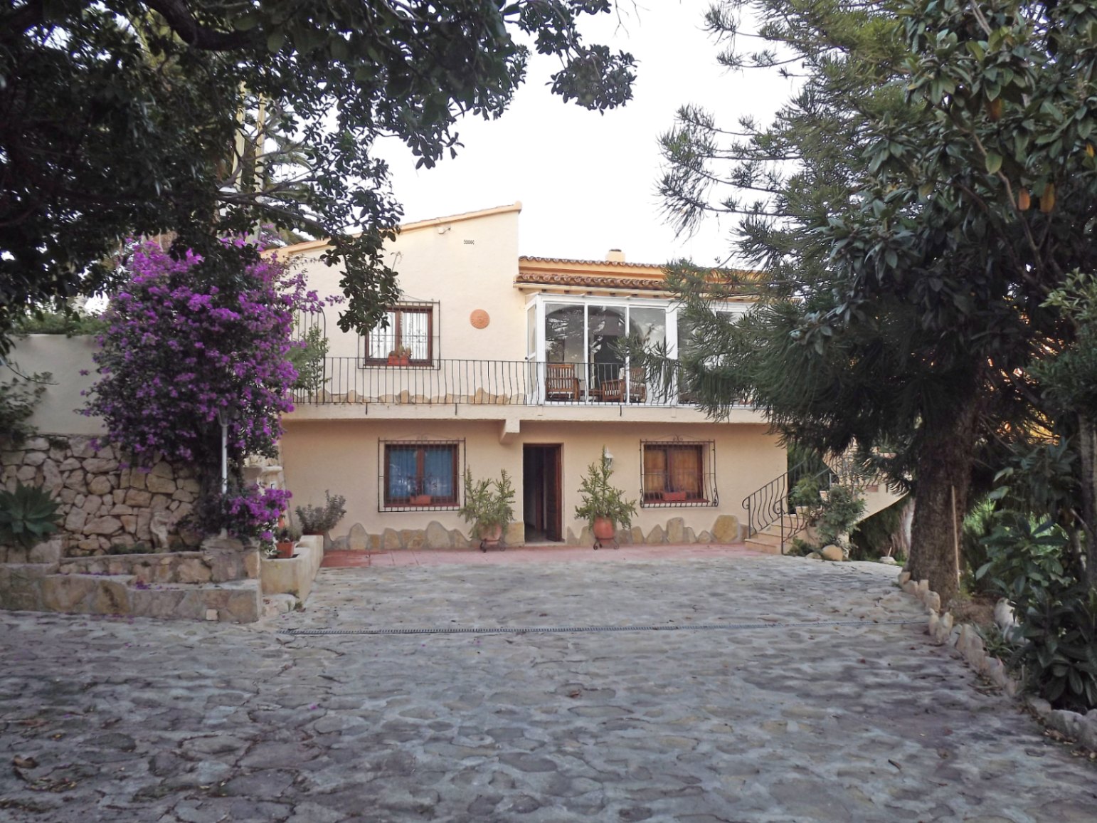 Voorgevel van de villa met een met natuursteen geplaveide oprit, een beglaasd terras op de bovenverdieping en authentieke mediterrane details.