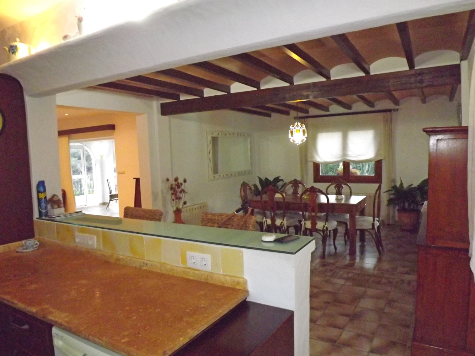 Zicht vanuit de keuken op de eethoek, met een plafond van houten balken en terracotta, keramische vloeren en een ontbijtbar met een natuurstenen werkblad.