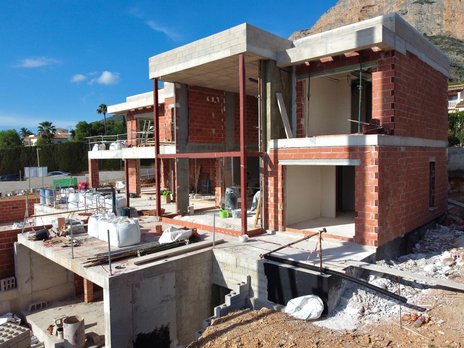 Huidige bouwfase van de villa, met de bakstenen structuur, betonnen vloeren en stalen steunbalken tegen de achtergrond van de Montgó-berg.