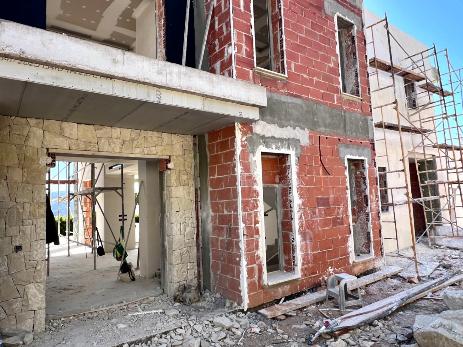 Huidige bouwstatus van de villa met rode bakstenen muren, natuurstenen gevelbekleding en betonnen constructie-elementen met steigers.