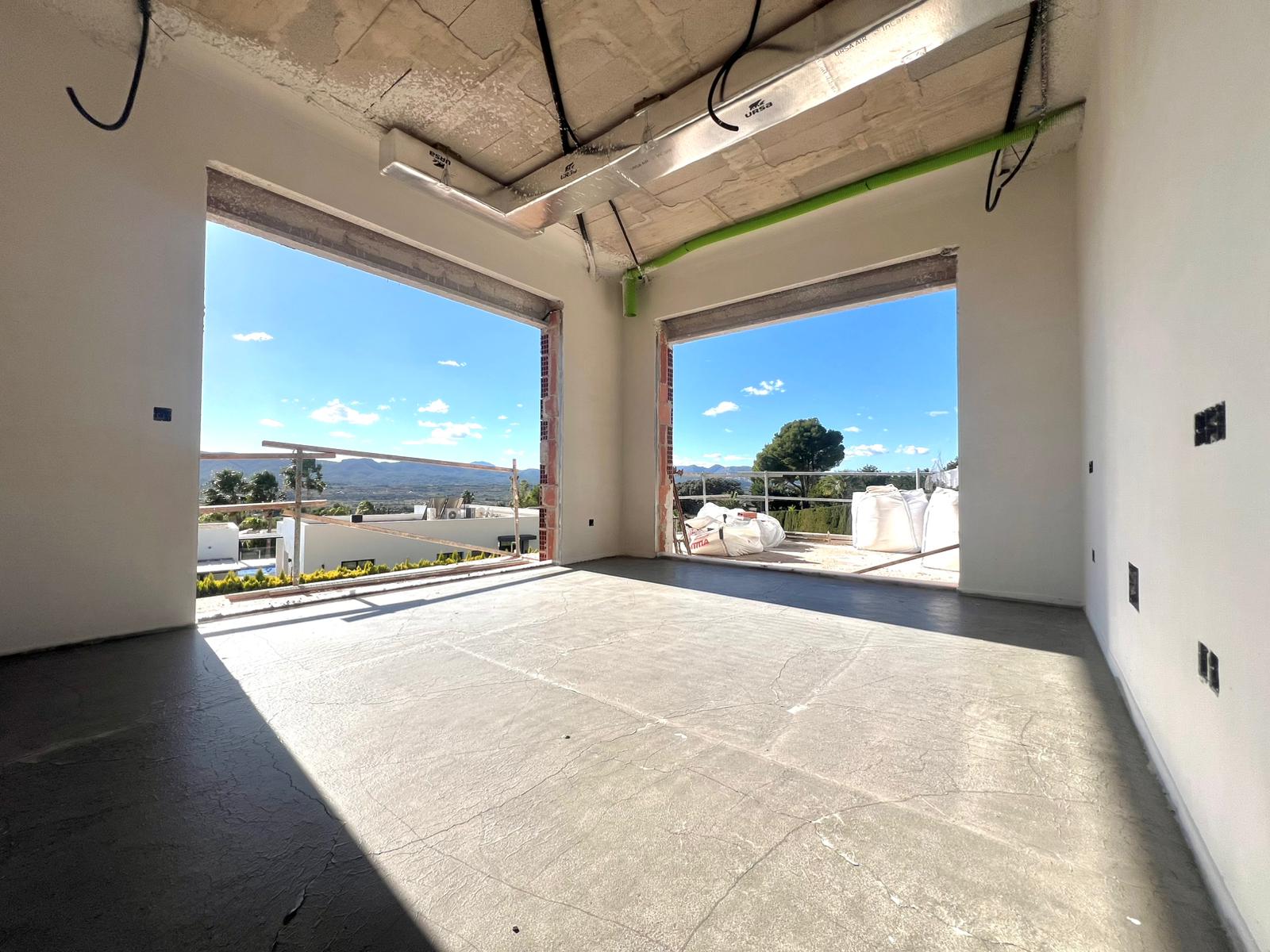 Interieur in ruwbouw met grote raamopeningen en panoramisch uitzicht, voorzien van zichtbare betonplafonds en airconditioningskanalen.