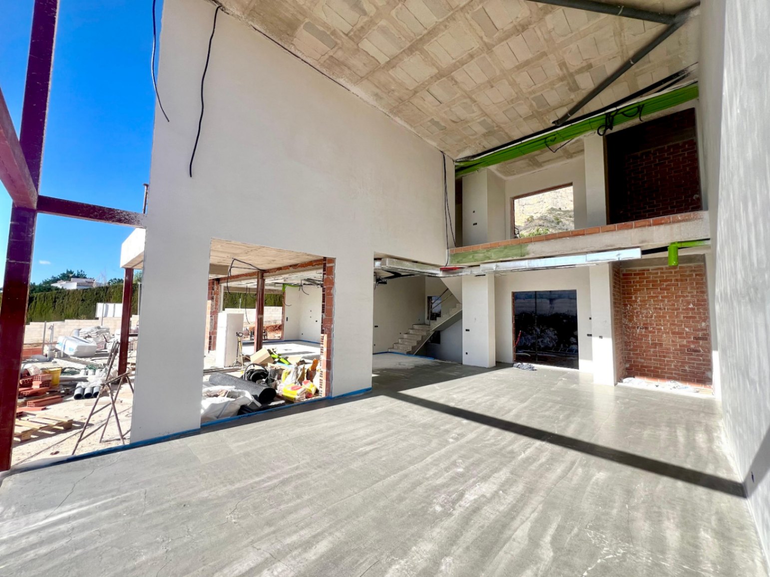 Interieur van de woonkamer met dubbele hoogte in aanbouw, met de open mezzanine, betonnen trap en grote openingen voor kamerhoge ramen.