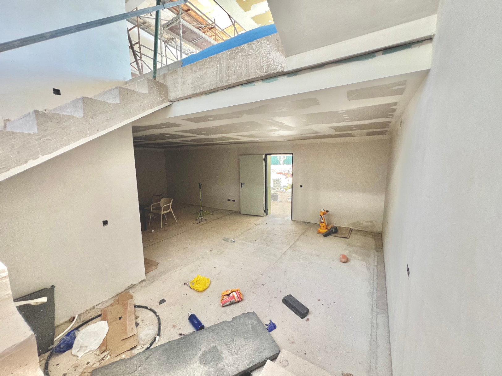 Interieurzicht van de benedenverdieping in ruwbouw met betonnen trap en een grote multifunctionele ruimte voor een fitness of bioscoop.