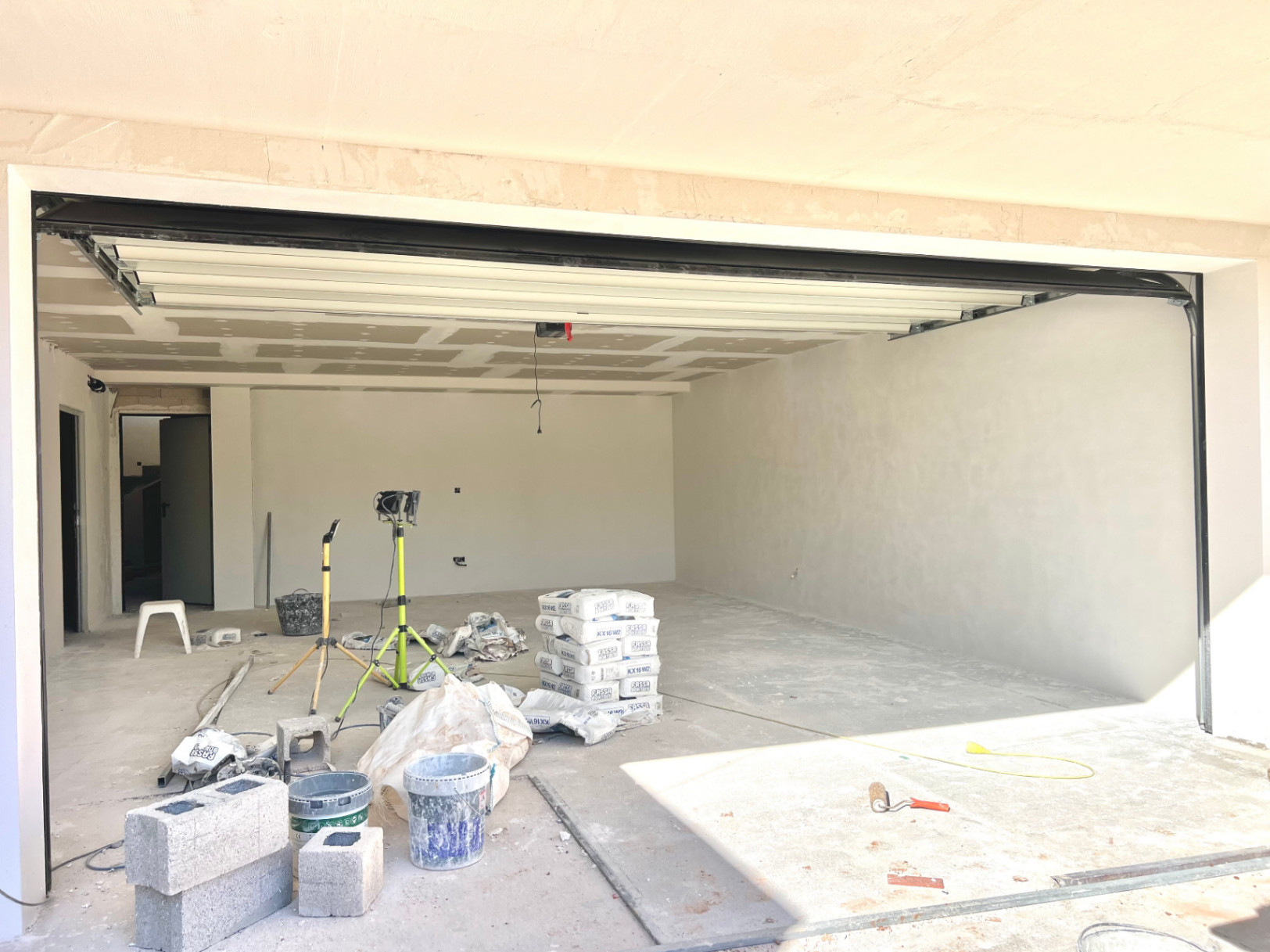 Ruime garage in aanbouw met witte sectionaaldeur, gestuukte muren en gipsplaten plafond, geschikt voor meerdere voertuigen of extra opslag.