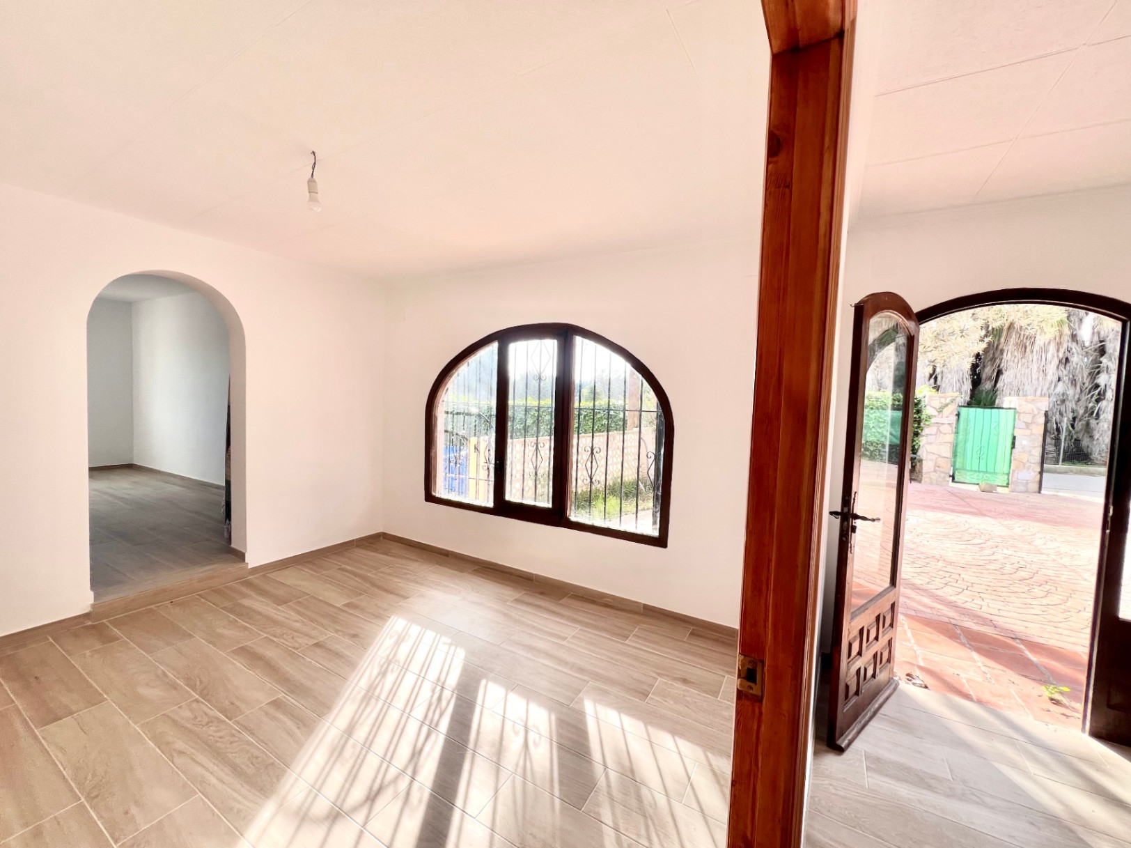 Lichte woonkamer met houtlook tegelvloer, een karakteristiek boogvenster en directe toegang tot het geplaveide terras.