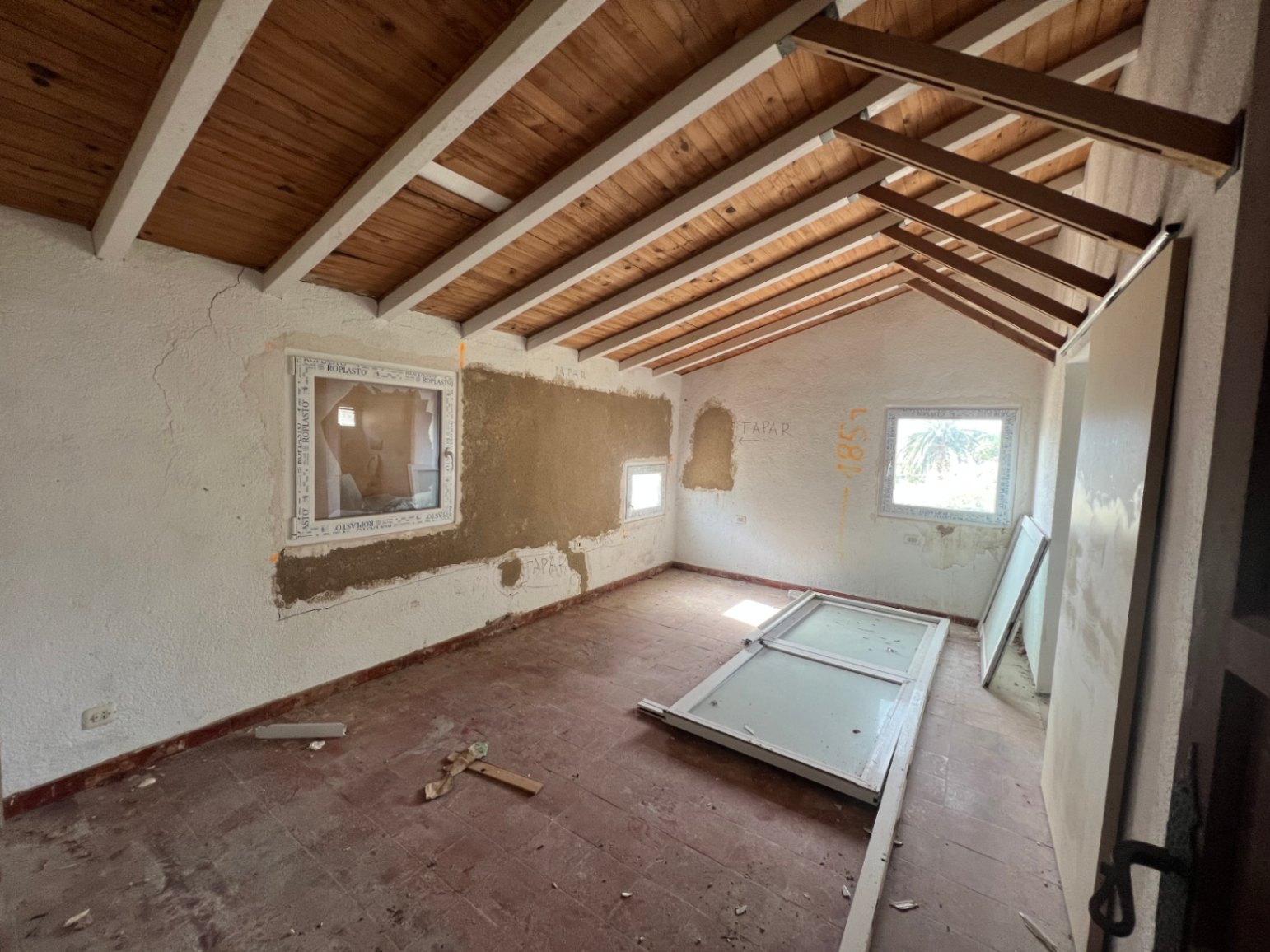 Binnenruimte in renovatie met authentieke terracotta vloeren, een zichtbaar houten balkenplafond en nieuw geplaatste PVC-kozijnen.