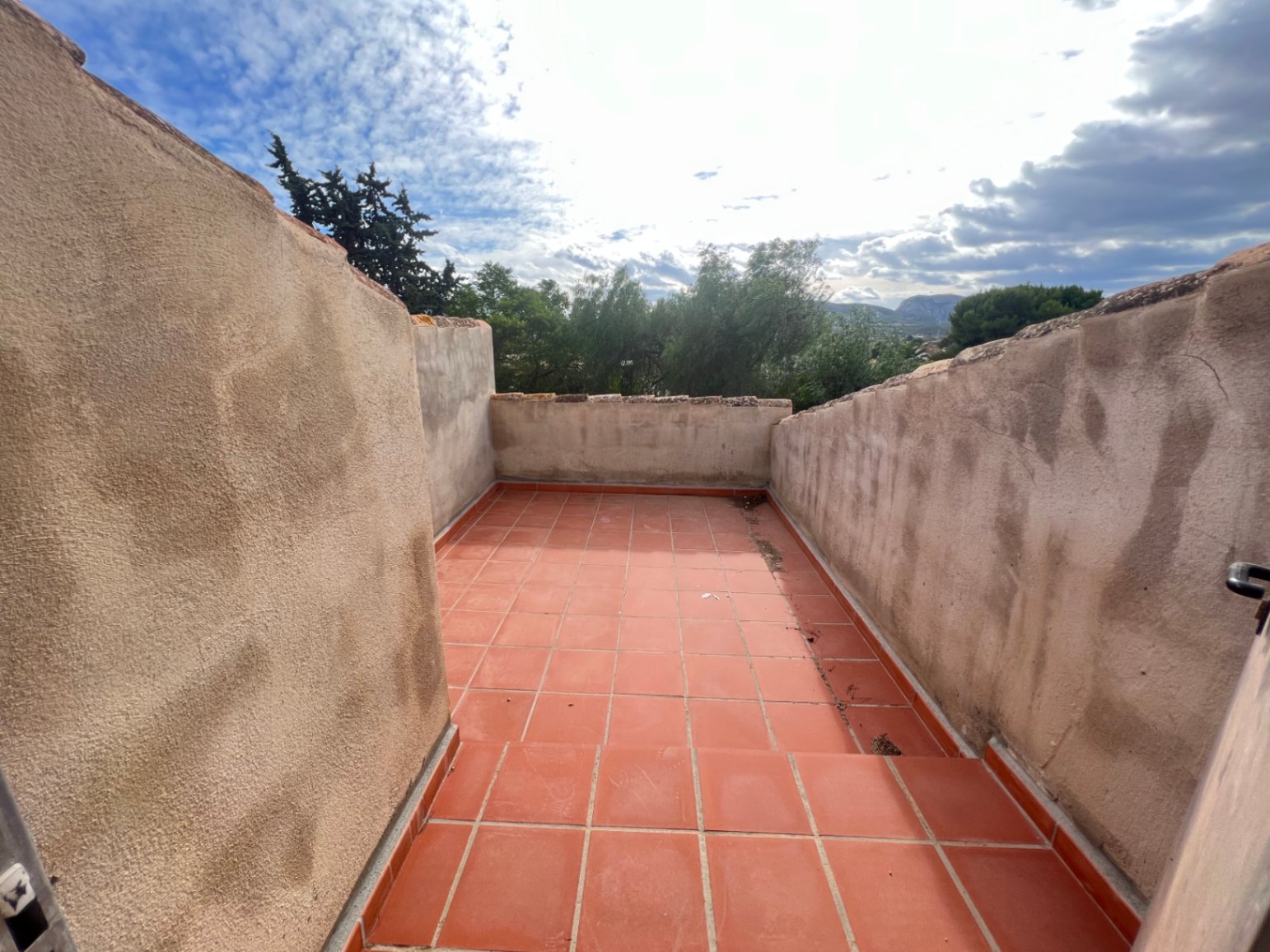 Dakterras op de bovenverdieping met terracotta vloertegels en hoge gestuukte muren, met vrij uitzicht over de boomtoppen en het omliggende berglandschap.