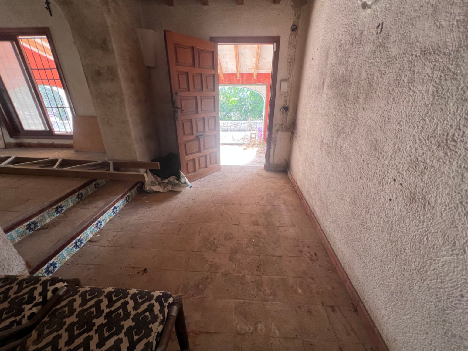 Entreehal met terracotta vloertegels, een houten paneeldeur en treden met traditionele siertegels, klaar voor een volledige renovatie in Jávea.