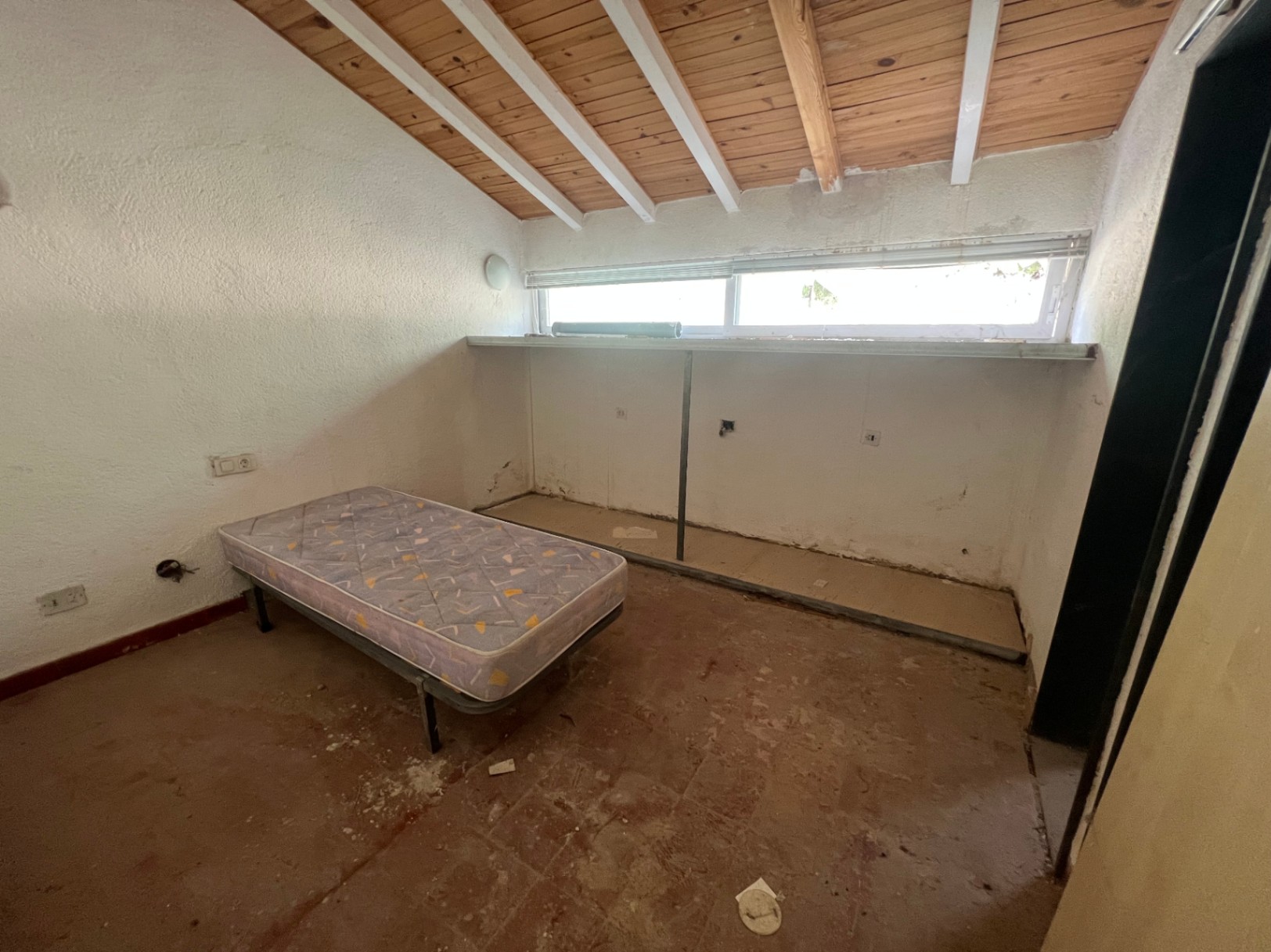 Slaapkamer met schuin plafond, houten balken en witte spanten. De ruimte is voorzien van originele terracotta tegels en een langwerpig horizontaal raam.
