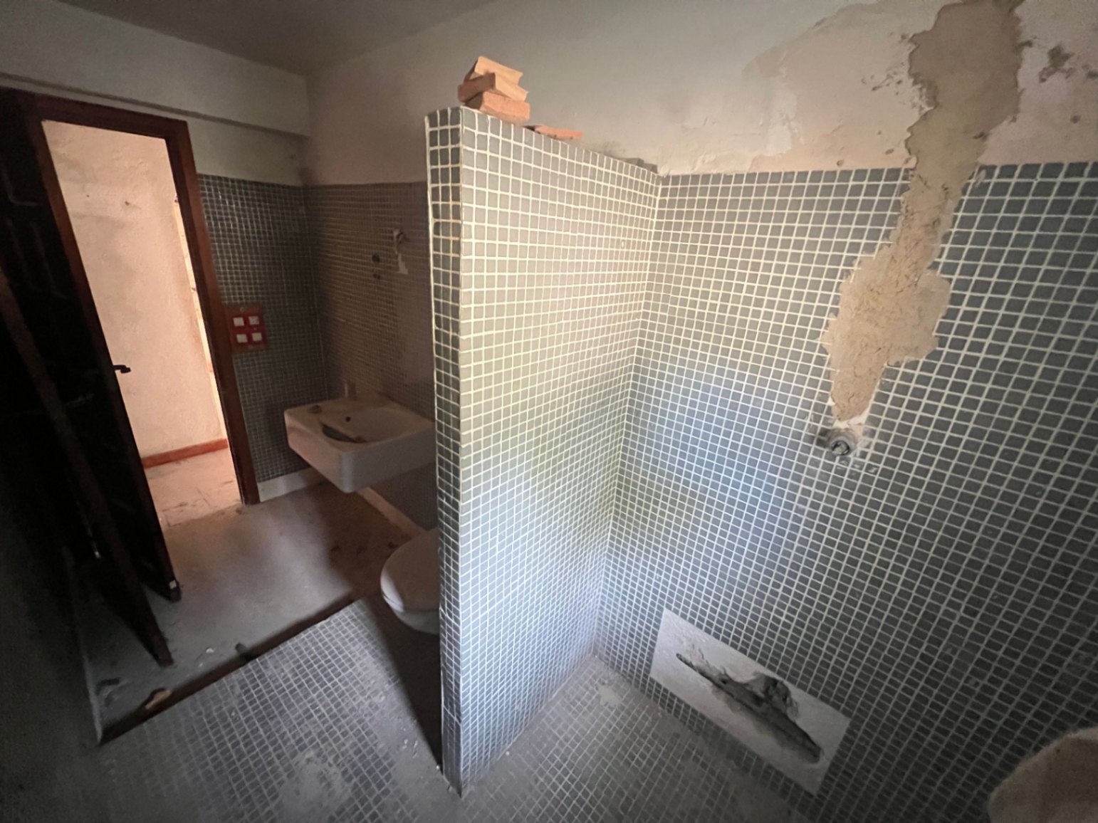 Te renoveren badkamer met blauwe mozaïektegels, een gemetselde douchewand en origineel sanitair, perfect voor een volledige modernisering naar eigen smaak.