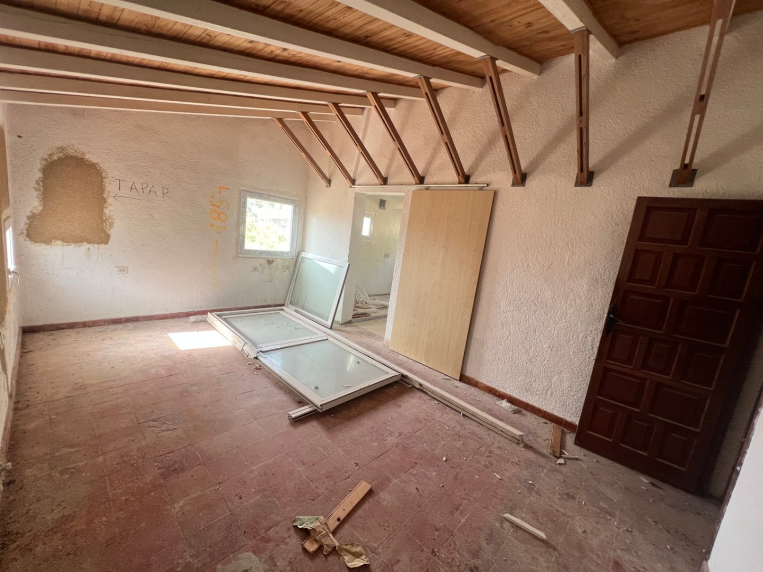 Te renoveren kamer met authentieke houten balkenplafonds, originele terracotta vloertegels en nieuwe raamkozijnen klaar voor installatie.