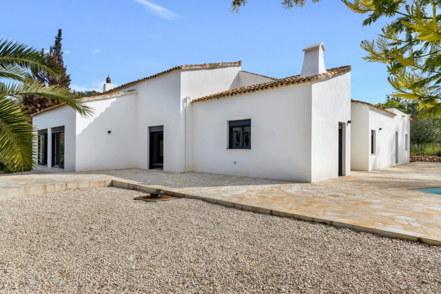 Buitenzicht van een mediterrane villa met witte stucwerkmuren, terracotta dakpannen en een ruim terras van natuursteen grenzend aan een grindgedeelte.