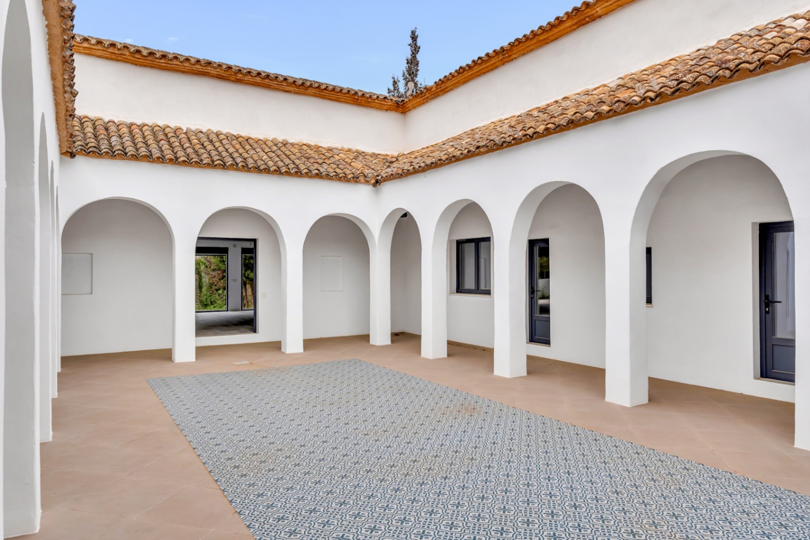 Centrale binnenplaats met witte bogen, terracotta dakpannen en een decoratieve tegelvloer met een centraal motief in een authentieke mediterrane stijl.