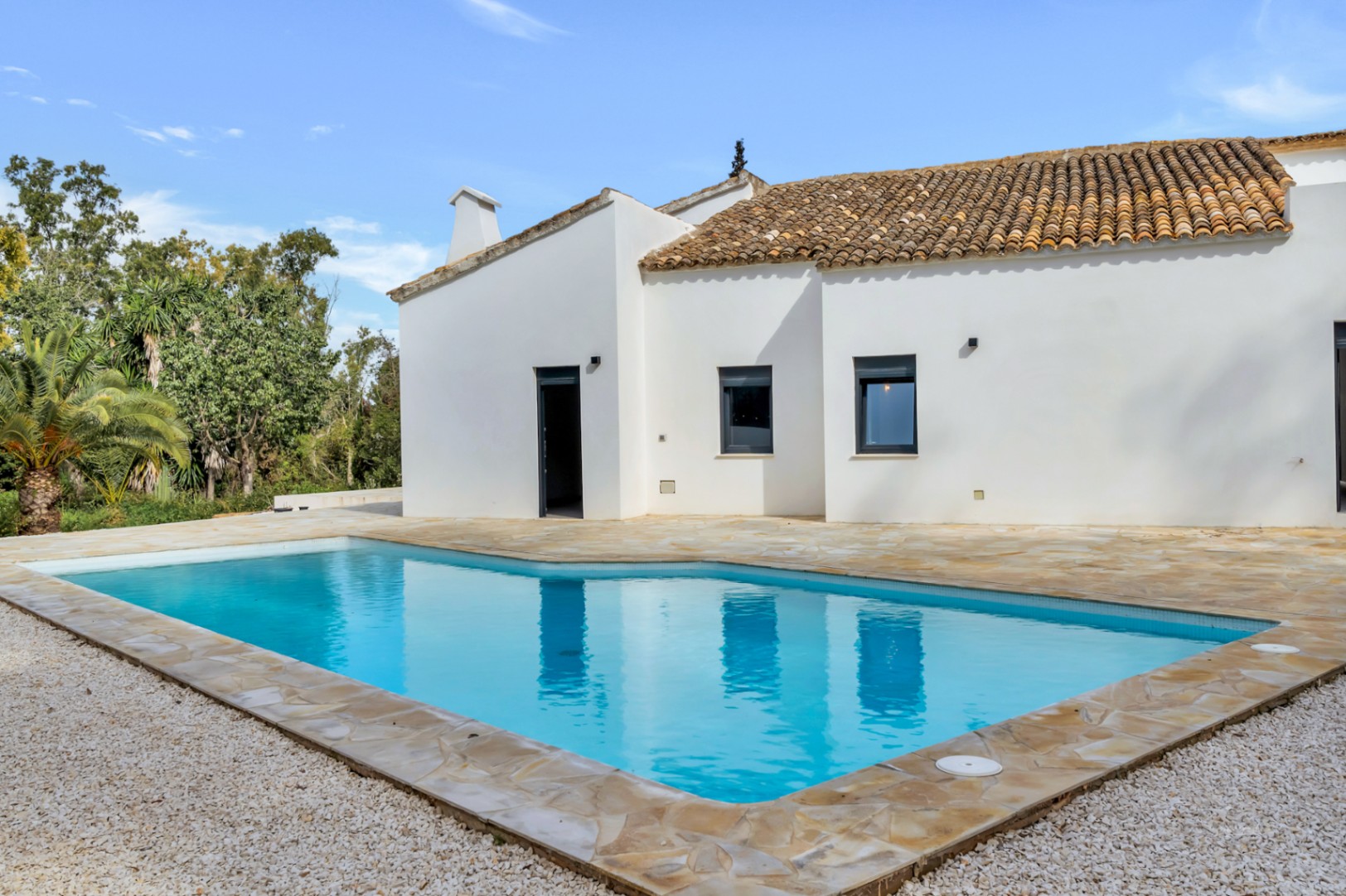 Exterieur van de villa met privézwembad omgeven door een natuurstenen terras en wit grind, met mediterrane architectuur met witte muren en terracotta dakpannen.