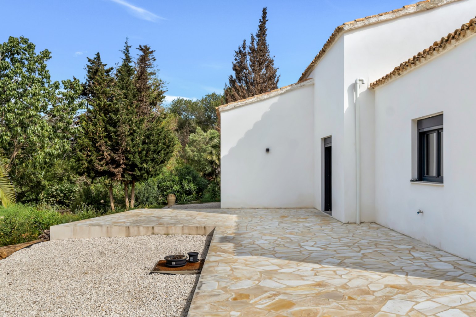 Exterieur van de villa met witte stucwerk gevels, terracotta dakpannen en een ruim terras van natuursteen omgeven door mediterrane begroeiing.
