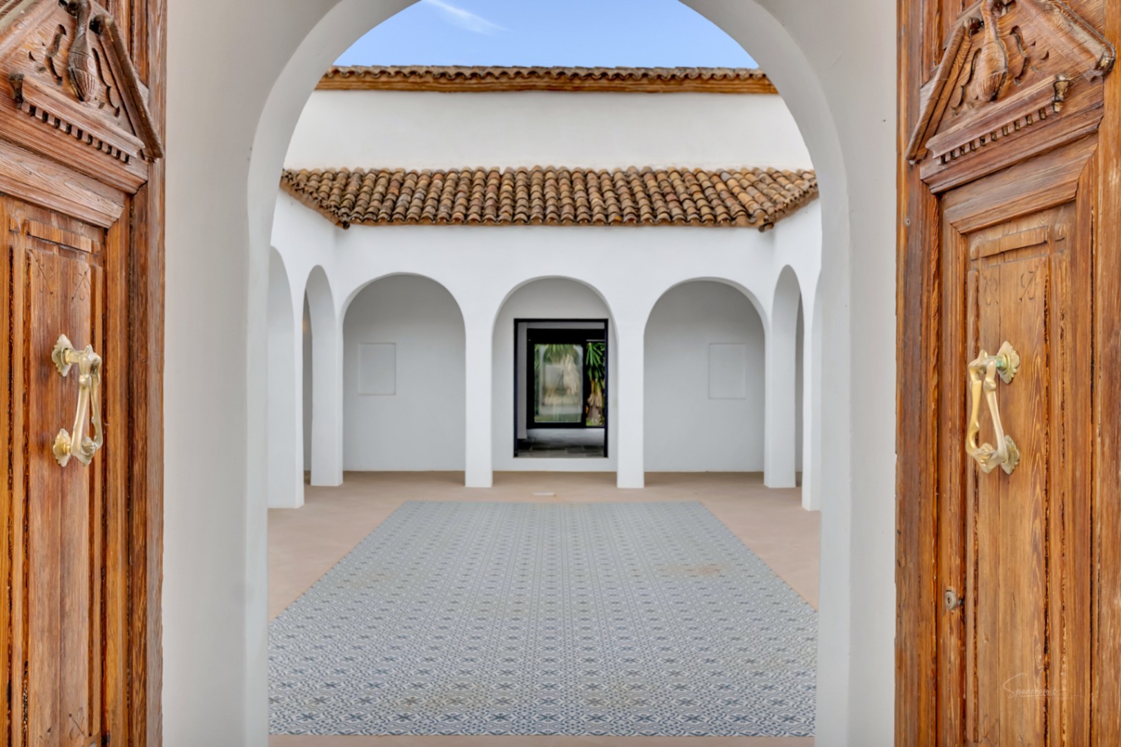 Mediterrane binnenplaats met witte bogen, gedecoreerde tegelvloer en authentieke houten deuren met koperen kloppers.