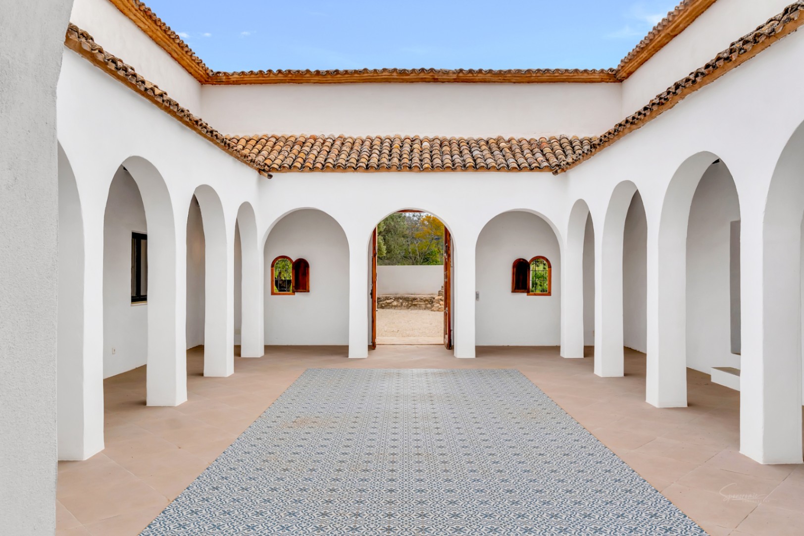 Mediterrane binnenplaats met witte bogen, terracotta dakpannen en een centraal vloergedeelte met decoratieve patroontegels in een open setting.