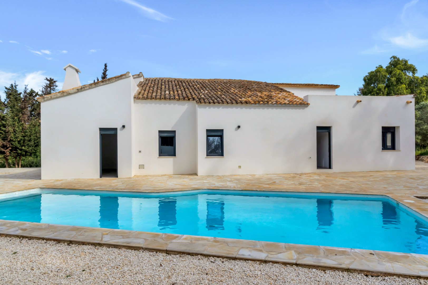 Mediterrane villa met witte muren, terracotta dakpannen en een zwembad omgeven door een natuurstenen terras en een grindgedeelte.