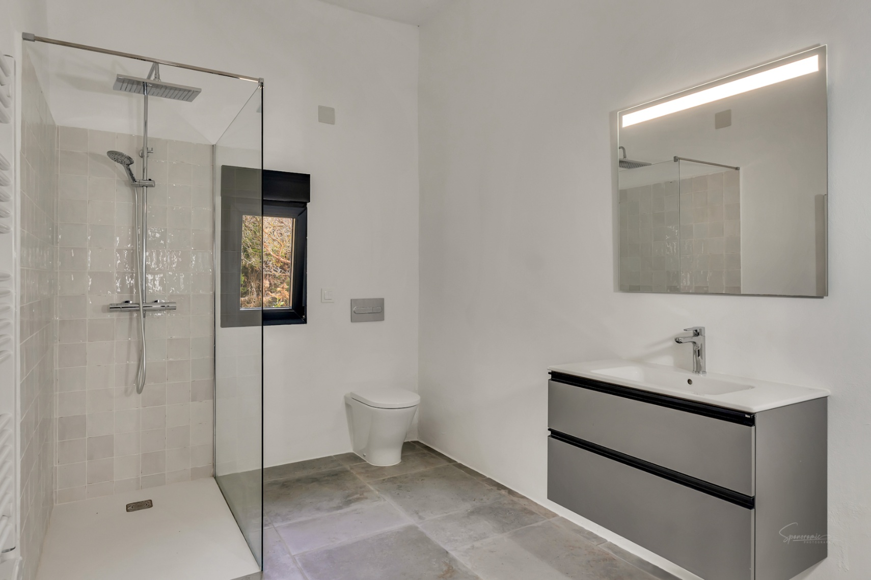 Moderne badkamer met inloopdouche, glazen wand en regendouche. Voorzien van een zwevend grijs wastafelmeubel, spiegel met verlichting en een karakteristieke stenen vloer.