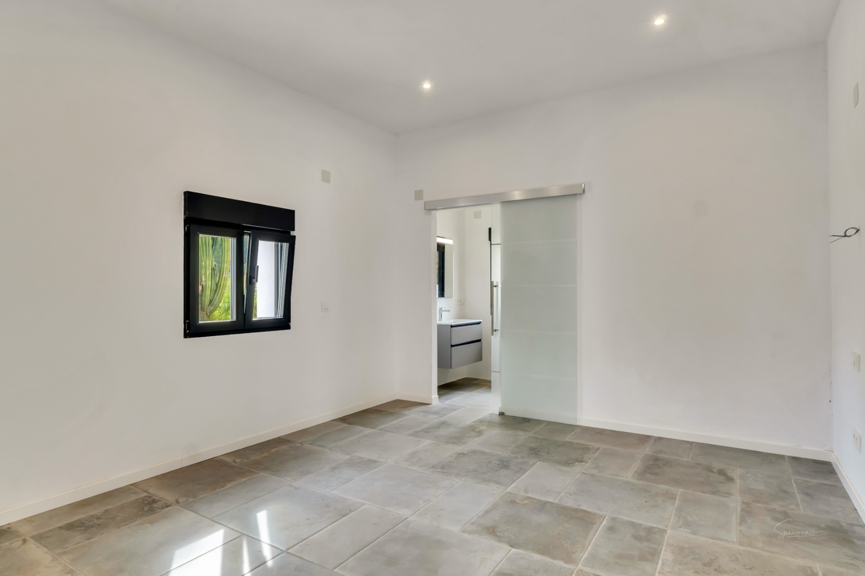 Slaapkamer met natuurstenen vloer, inbouwspots en een matglazen schuifdeur die toegang biedt tot de moderne en-suite badkamer.