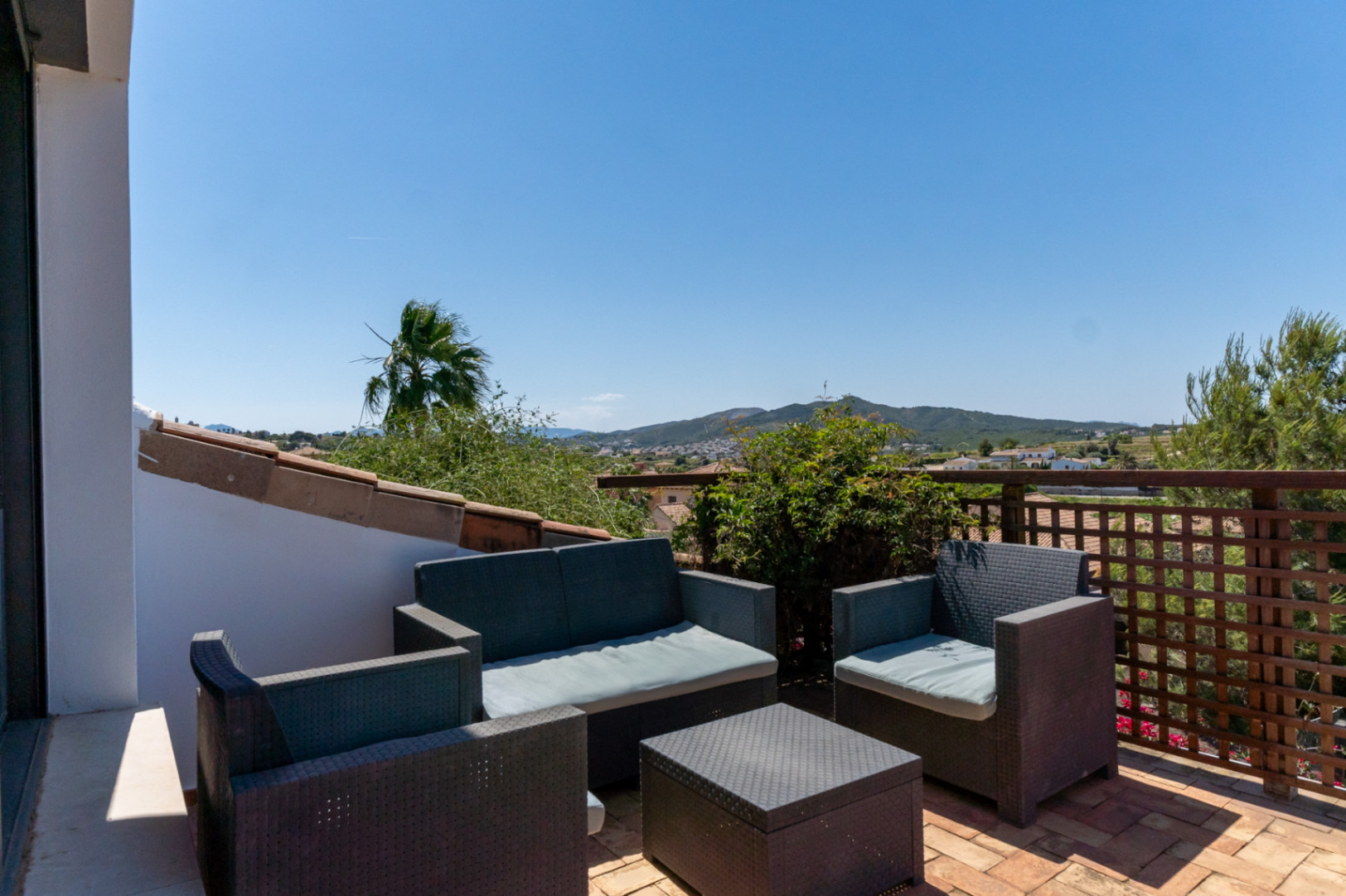 Bovenste terras met een loungeset van kunstrotan en terracotta tegels, met vrij uitzicht over de vallei en de bergen van Jávea.