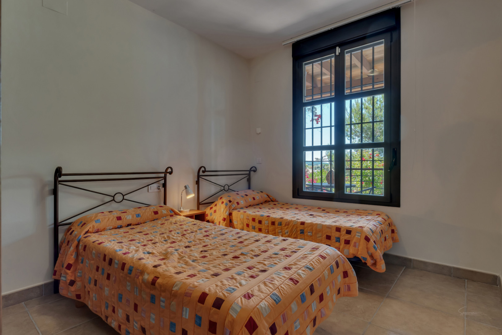 Lichte slaapkamer met twee eenpersoonsbedden, smeedijzeren hoofdeinden en een raam met uitzicht op de omliggende tuin.