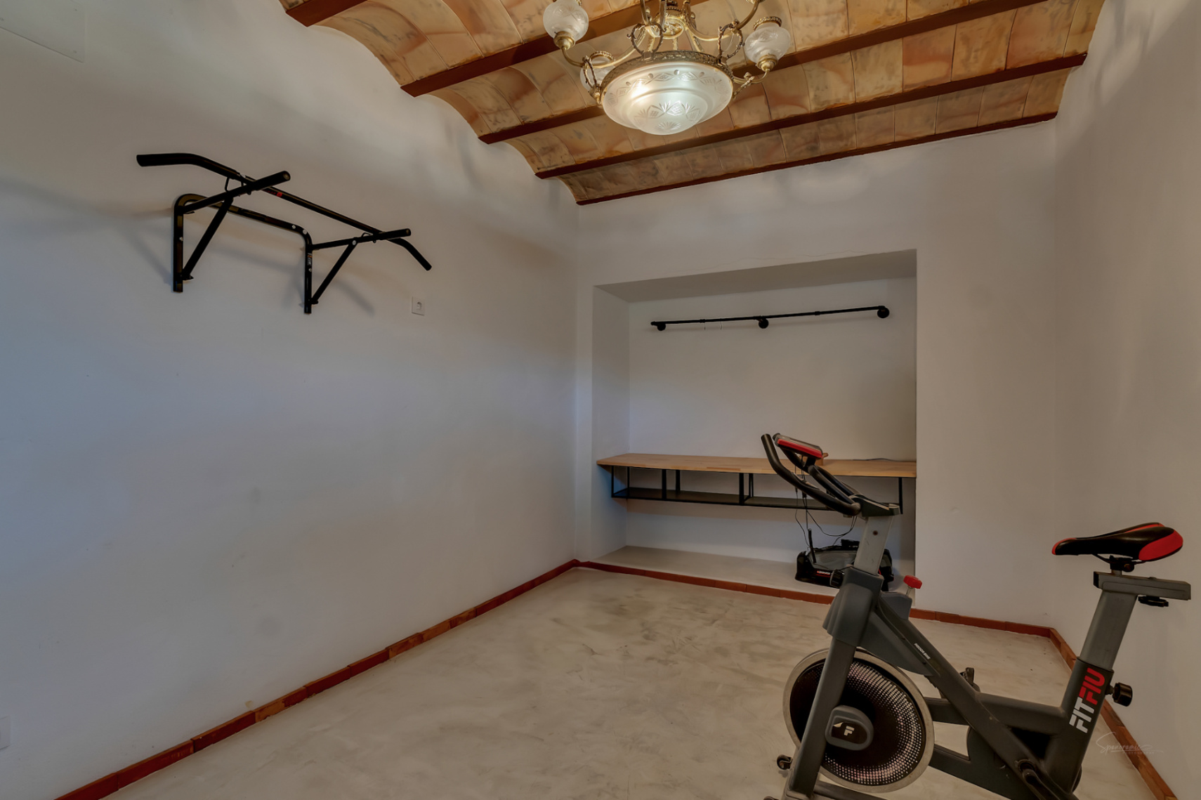Multifunctionele fitnessruimte met traditionele gewelfde plafonds, wandmontage optrekstang, hometrainer en een ingebouwde bureau-nis.