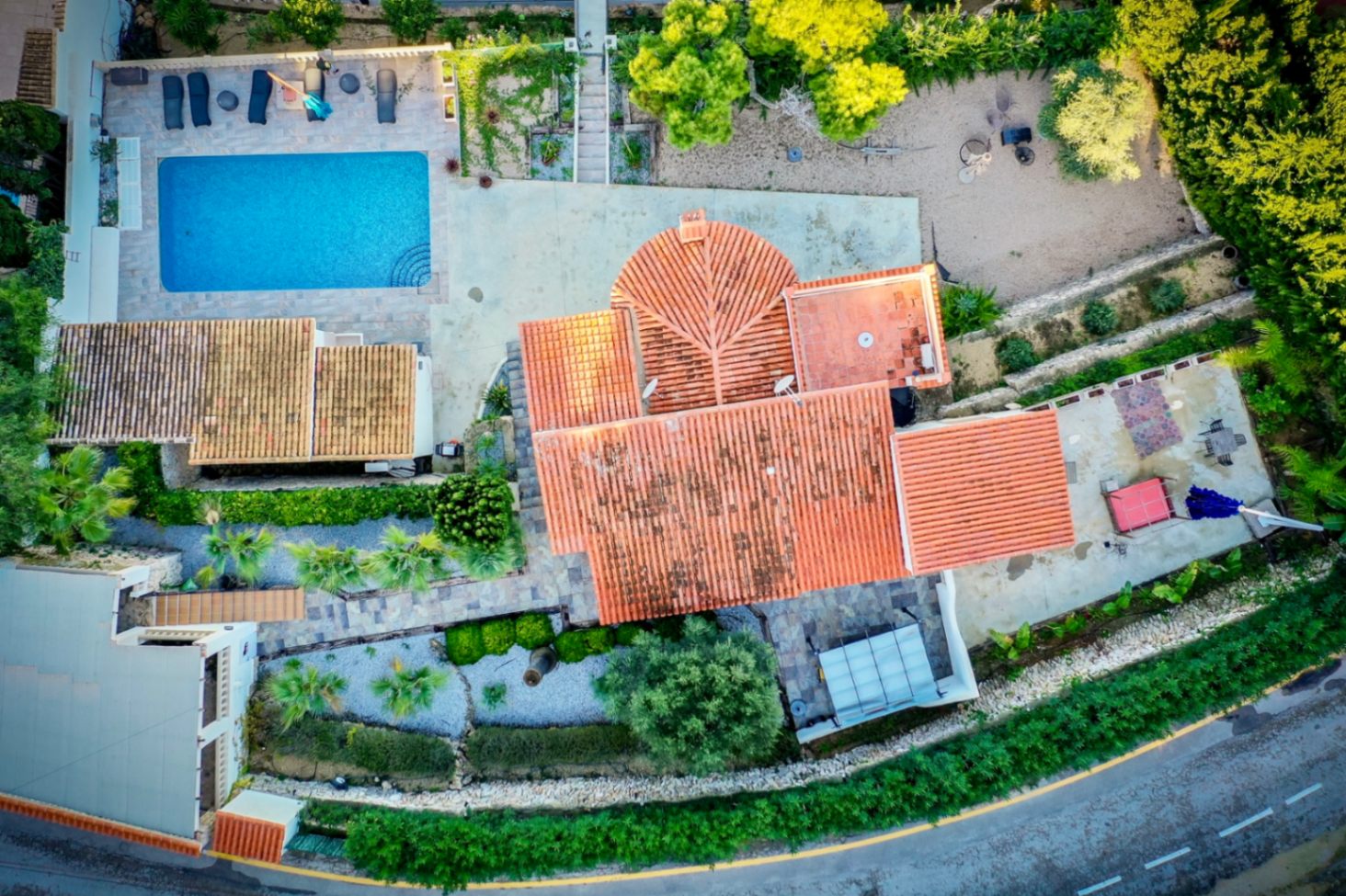 Bovenaanzicht van de villa met het rechthoekige zwembad, het zonneterras en het traditionele pannendak, gelegen op een perceel met mediterrane beplanting.
