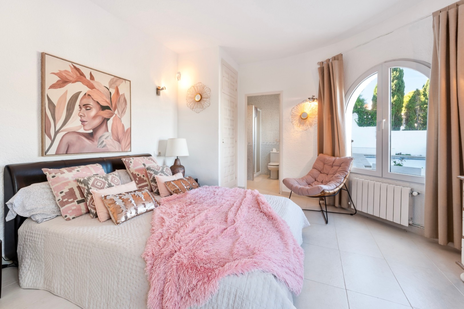 Lichte slaapkamer met en-suite badkamer, een boogvenster met zicht op het zwembad en een eigentijdse inrichting met warme tinten en tegelvloer.